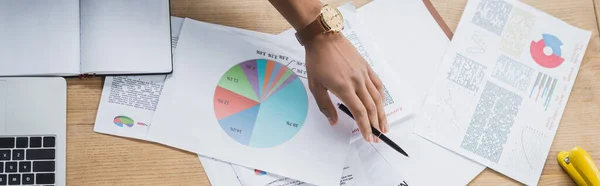 Ansicht von afrikanisch-amerikanischem Geschäftsmann mit Stift in der Nähe von Dokumenten mit Diagrammen und Laptop im Büro, Banner — Stockfoto