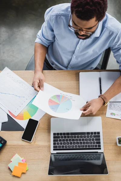 Overhead-Ansicht von jungen afrikanisch-amerikanischen Geschäftsmann hält Dokument in der Nähe von Geräten mit leerem Bildschirm im Büro — Stockfoto