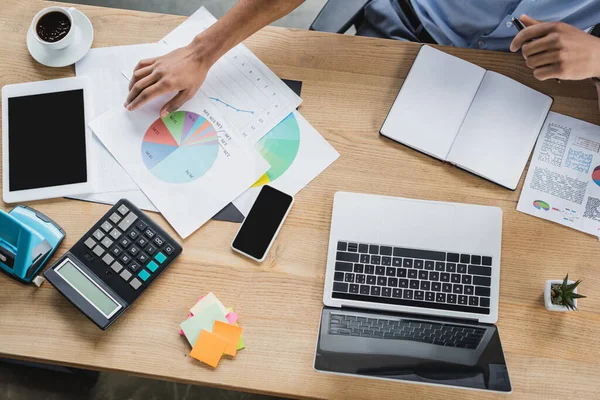 Top view of african american businessman taking document near devices and calculator in office — Stock Photo