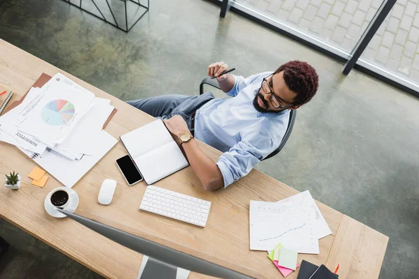 Overhead view of african american businessman looking at computer monitor near papers on table — Stock Photo