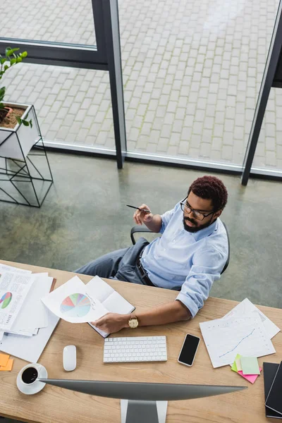 Overhead-Ansicht eines afrikanisch-amerikanischen Managers, der im Büro mit Computer und Dokumenten bei einer Tasse Kaffee arbeitet — Stockfoto