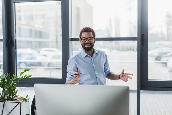 Glücklicher afrikanisch-amerikanischer Geschäftsmann mit Stift blickt im Büro auf Computermonitor — Stockfoto