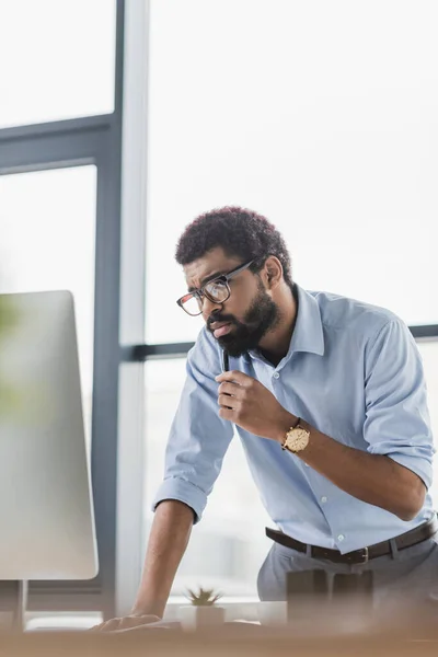 Gerente afroamericano sosteniendo pluma mientras usa computadora en la oficina - foto de stock