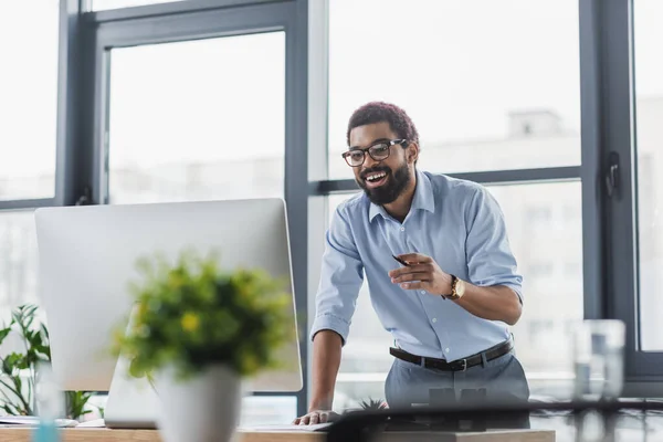 Positiver afrikanisch-amerikanischer Geschäftsmann mit Brille blickt im Büro auf Computermonitor — Stockfoto