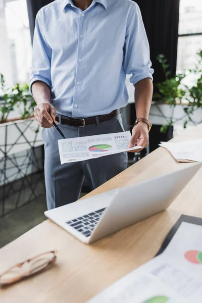 Cropped view of african american businessman holding document near laptop in office — Stock Photo