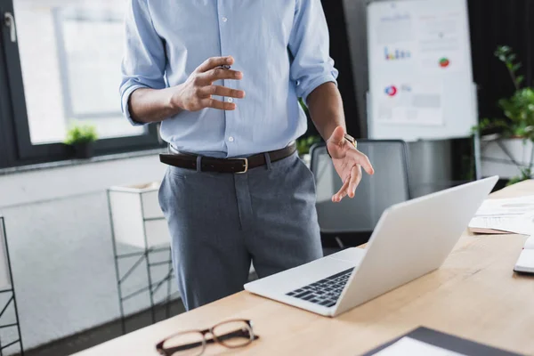 Cropped view of african american businessman gesturing near laptop and eyeglasses in office — Stock Photo