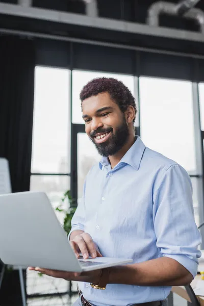 Sorrindo empresário afro-americano usando laptop no escritório — Fotografia de Stock