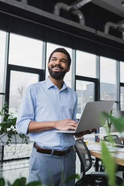 Positiver afrikanisch-amerikanischer Geschäftsmann nutzt Laptop und schaut im Büro weg — Stockfoto