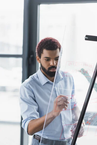 Un homme d'affaires afro-américain écrit sur un panneau de verre au bureau — Photo de stock