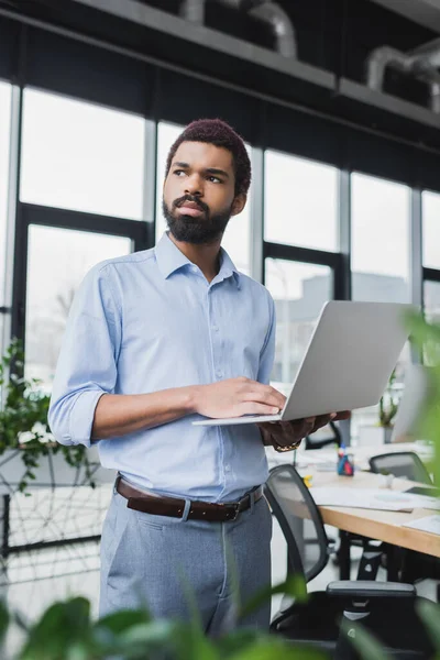 Pensativo hombre de negocios afroamericano utilizando portátil en la oficina - foto de stock