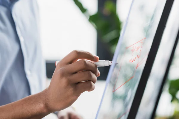 Ausgeschnittene Ansicht eines afrikanisch-amerikanischen Geschäftsmannes, der im Büro auf Glastafel schreibt — Stockfoto