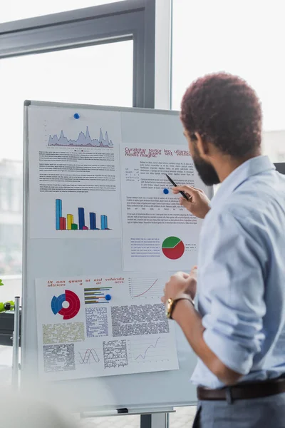 Blurred african american businessman standing near flip chart with graphs in office — Stock Photo