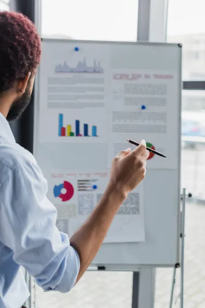 Afrikanischer Geschäftsmann hält Stift in der Nähe von verschwommenem Flipchart im Büro — Stockfoto