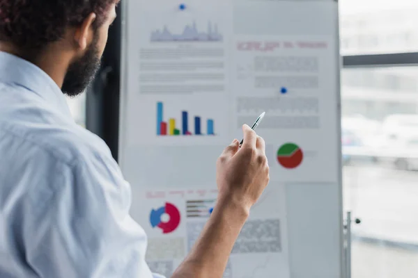 Pen in hand of african american businessman near blurred flip chart in office — Stock Photo