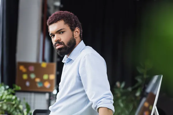 Un homme d'affaires afro-américain regardant une caméra près d'un écran d'ordinateur au bureau — Photo de stock