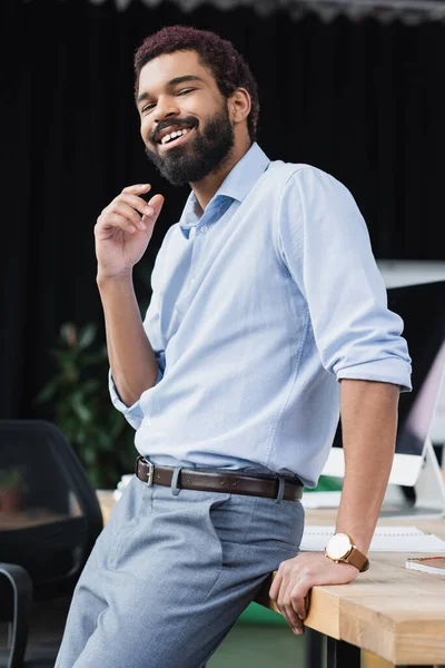 Fröhlicher afrikanisch-amerikanischer Geschäftsmann blickt im Büro in die Kamera am Arbeitstisch — Stockfoto