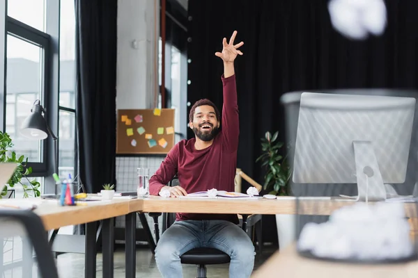 Smiling african american businessman throwing crumpled paper in trash can in office — Stock Photo