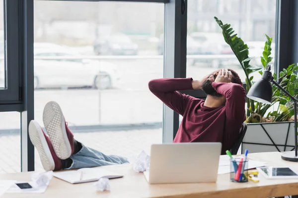 Hombre de negocios afroamericano cansado sentado cerca de dispositivos y papel arrugado en la oficina - foto de stock