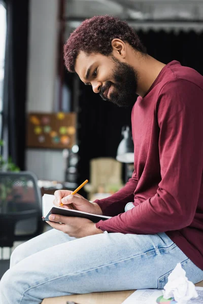 Young african american businessman in casual clothes writing on notebook in office — Stock Photo