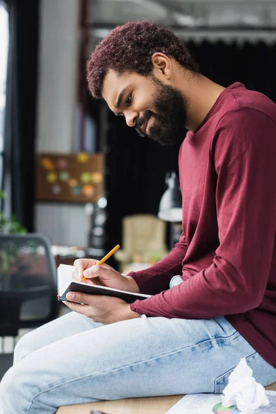 Joven hombre de negocios afroamericano en ropa casual escribiendo en un cuaderno en la oficina - foto de stock