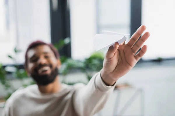 Paper plane in hand of blurred african american businessman in office — Stock Photo