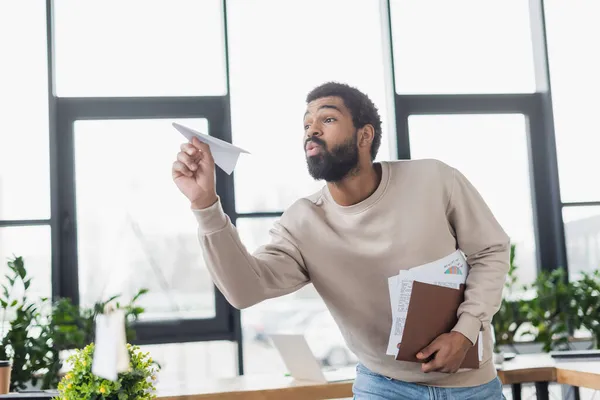 Young african american businessman holding paper folder and toy plane in office — Stock Photo