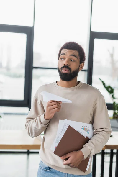 Junger afrikanisch-amerikanischer Geschäftsmann mit Papierflugzeug und Dokumenten im Amt — Stockfoto