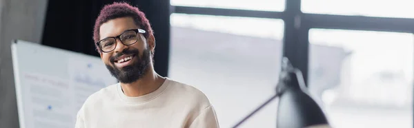 Sonriente hombre de negocios afroamericano en gafas mirando a la cámara en la oficina, pancarta - foto de stock