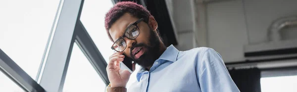 Низький кут Вид на афроамериканського бізнесмена, який розмовляє по мобільному в офісі, банер — стокове фото