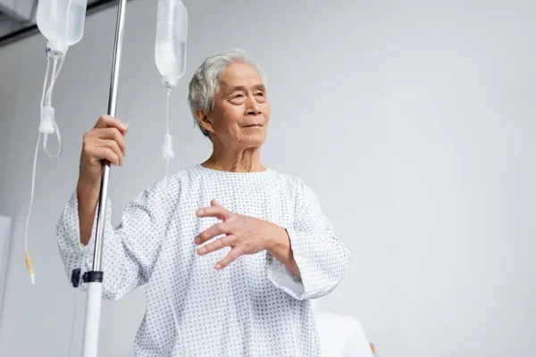 Elderly asian patient holding stand with intravenous therapy in hospital — Stock Photo