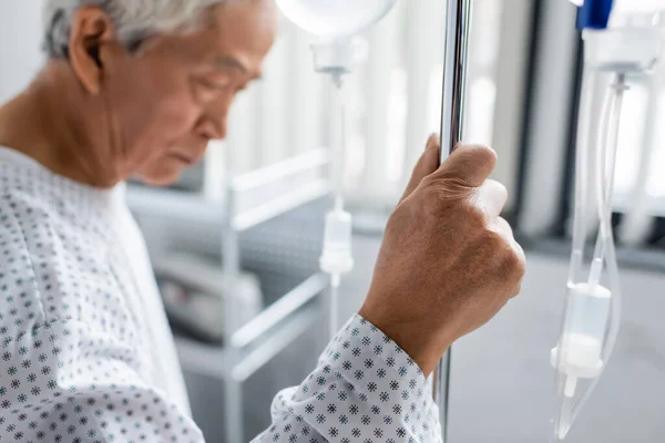 Desfocado ásia paciente segurando stand com intravenosa terapia no hospital ward — Fotografia de Stock