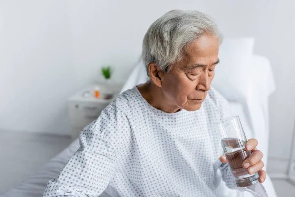 Elderly asian patient holding glass of water in hospital ward — Stock Photo