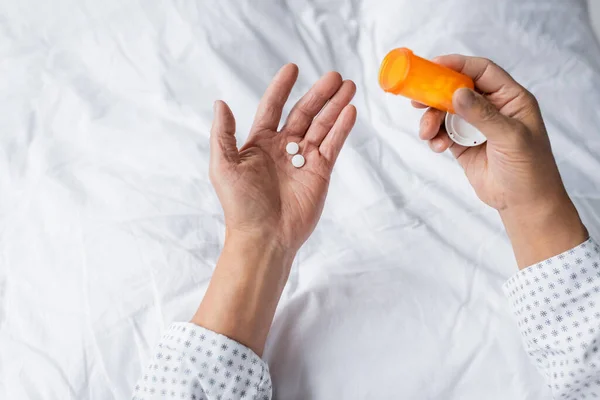 Vista cortada de homem idoso segurando frasco com pílulas na cama na clínica — Stock Photo