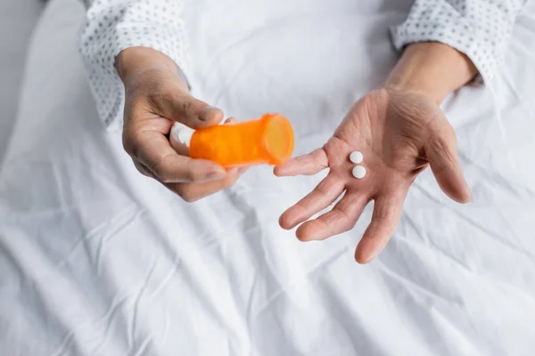 Cropped view of senior patient holding pills on bed in hospital — Stock Photo