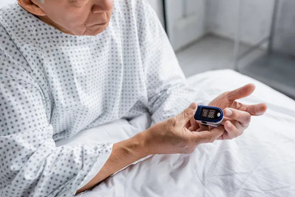 Cropped view of senior patient fastening pulse oximeter on bed in clinic — Stock Photo