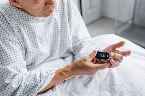 Vue recadrée de l'oxymètre de pouls de fixation du patient âgé sur le lit de la clinique — Photo de stock