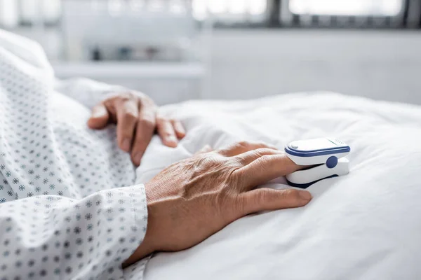 Cropped view of pulse oximeter on hand of elderly patient in hospital ward — Stock Photo