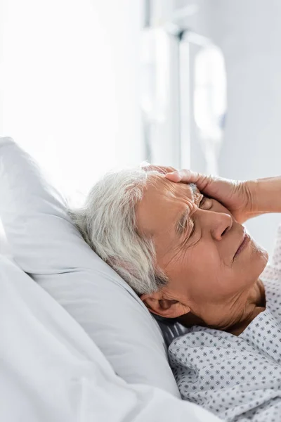 Patient asiatique âgé souffrant de maux de tête au lit en clinique — Photo de stock