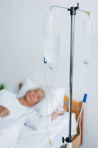 Intravenous therapy stand near blurred patient on bed in hospital — Stock Photo