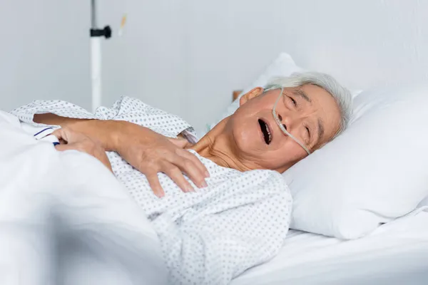 Enfermo paciente asiático con cánula nasal y oxímetro de pulso acostado en la cama del hospital - foto de stock