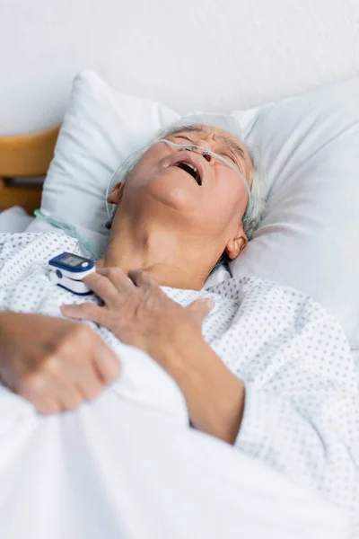 Diseased asian patient with pulse oximeter and nasal cannula lying on bed in clinic — Stock Photo