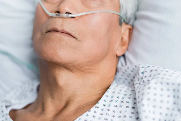 Vue recadrée d'un patient lisse avec une canule nasale couchée sur le lit à l'hôpital — Photo de stock