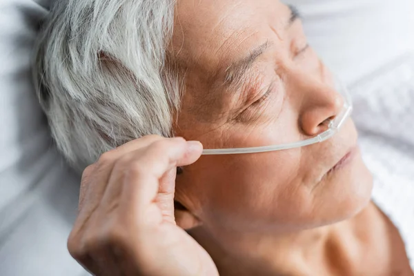 Elderly asian patient with nasal cannula lying with closed eyes on bed in clinic — Stock Photo