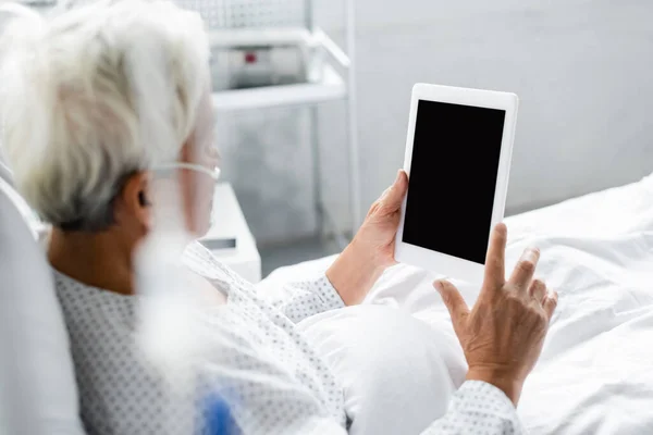 Paciente asiático borroso con cánula nasal sosteniendo tableta digital con pantalla en blanco en la cama en la clínica - foto de stock