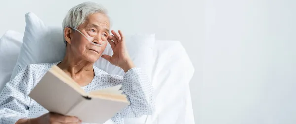 Anciano asiático paciente con nasal cánula celebración libro en hospital cama, bandera - foto de stock