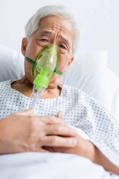 Ancianos asiático paciente en oxígeno máscara buscando en cámara en cama en clínica - foto de stock