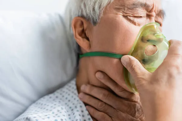 Enfermo asiático paciente en oxígeno máscara sentado en cama en hospital - foto de stock