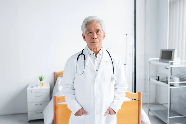Asiatique médecin dans blanc manteau regarder caméra dans hôpital salle — Photo de stock