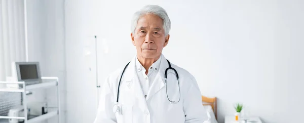 Médecin asiatique senior regardant la caméra à la clinique, bannière — Photo de stock
