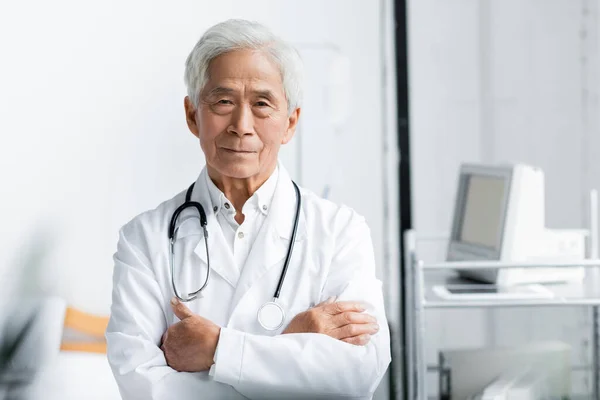 Senior asian doctor standing with crossed arms in hospital — Stock Photo